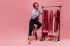 slim-lady-fashionable-trousers-blouse-red-hat-is-sitting-chair-stand-with-shiny-dresses_197531-17615