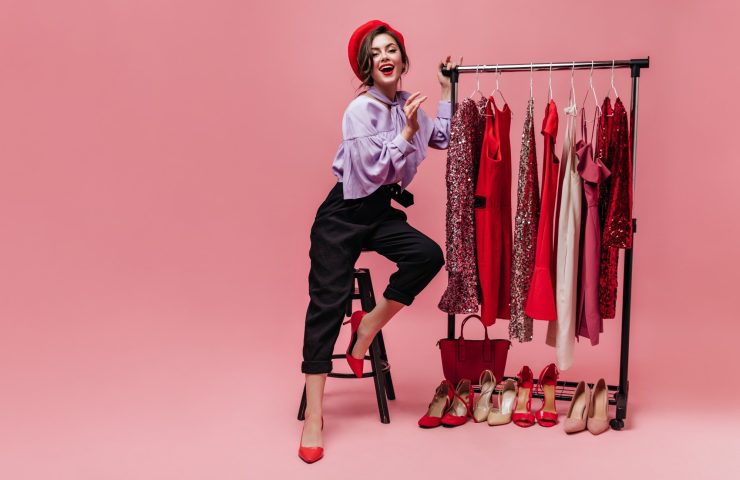 slim-lady-fashionable-trousers-blouse-red-hat-is-sitting-chair-stand-with-shiny-dresses_197531-17615